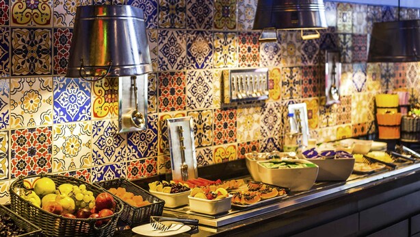 A buffet with various food items and utensils, a tiled backsplash, and hanging utensils.