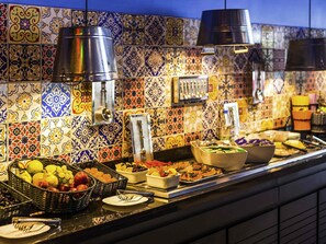 A buffet with various food items and utensils, a tiled backsplash, and hanging utensils. - ibis Styles Porto Alegre Centro (Porto Alegre)