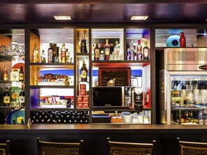 Uma área de bar com prateleiras de garrafas de bebidas, uma máquina de café e uma geladeira.