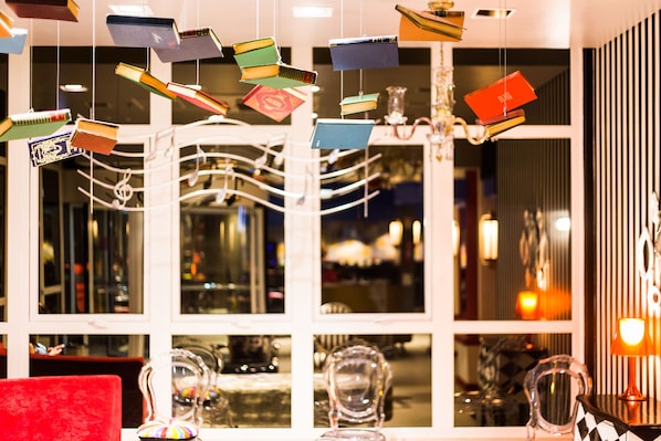 A room with a large window, a chandelier, and hanging books. - ibis Styles Porto Alegre Centro (Porto Alegre)