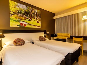 Habitación de hotel con dos camas, un escritorio, una silla y un cuadro grande que muestra un parque.