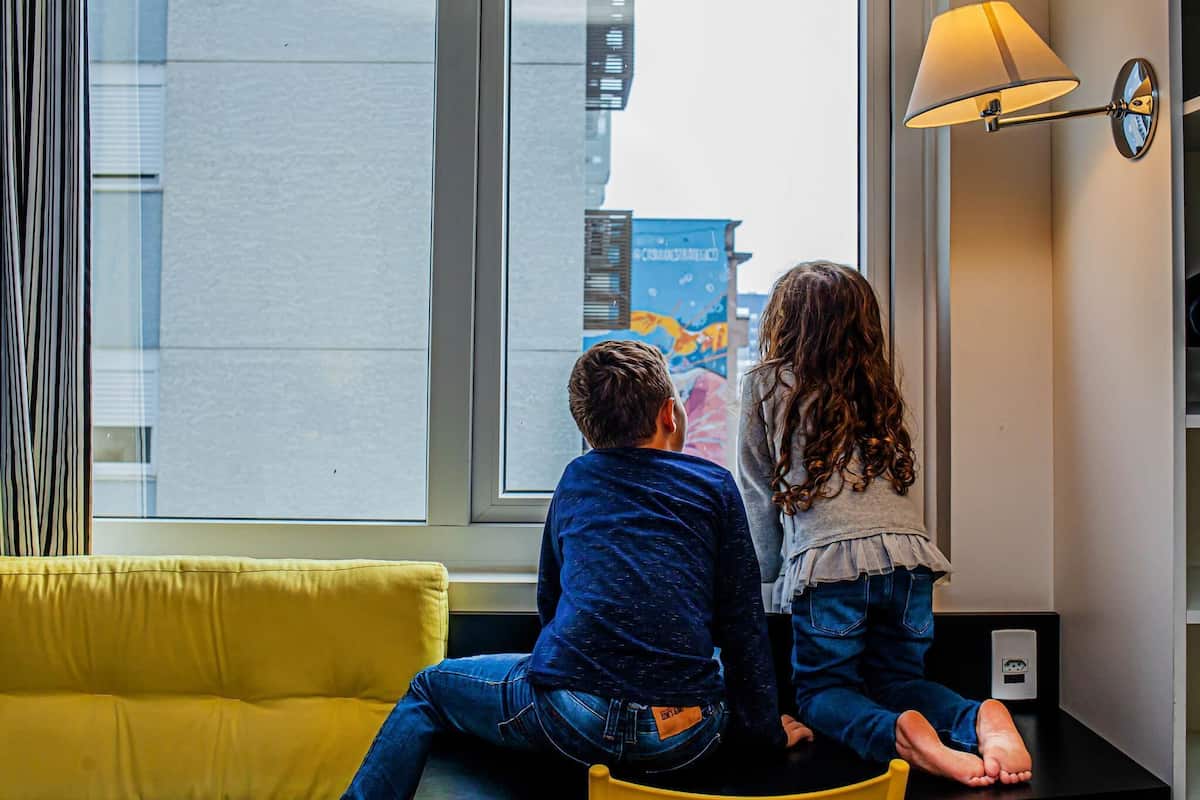 Quarto com sofá amarelo, mesa preta e janela com vista para edifícios.