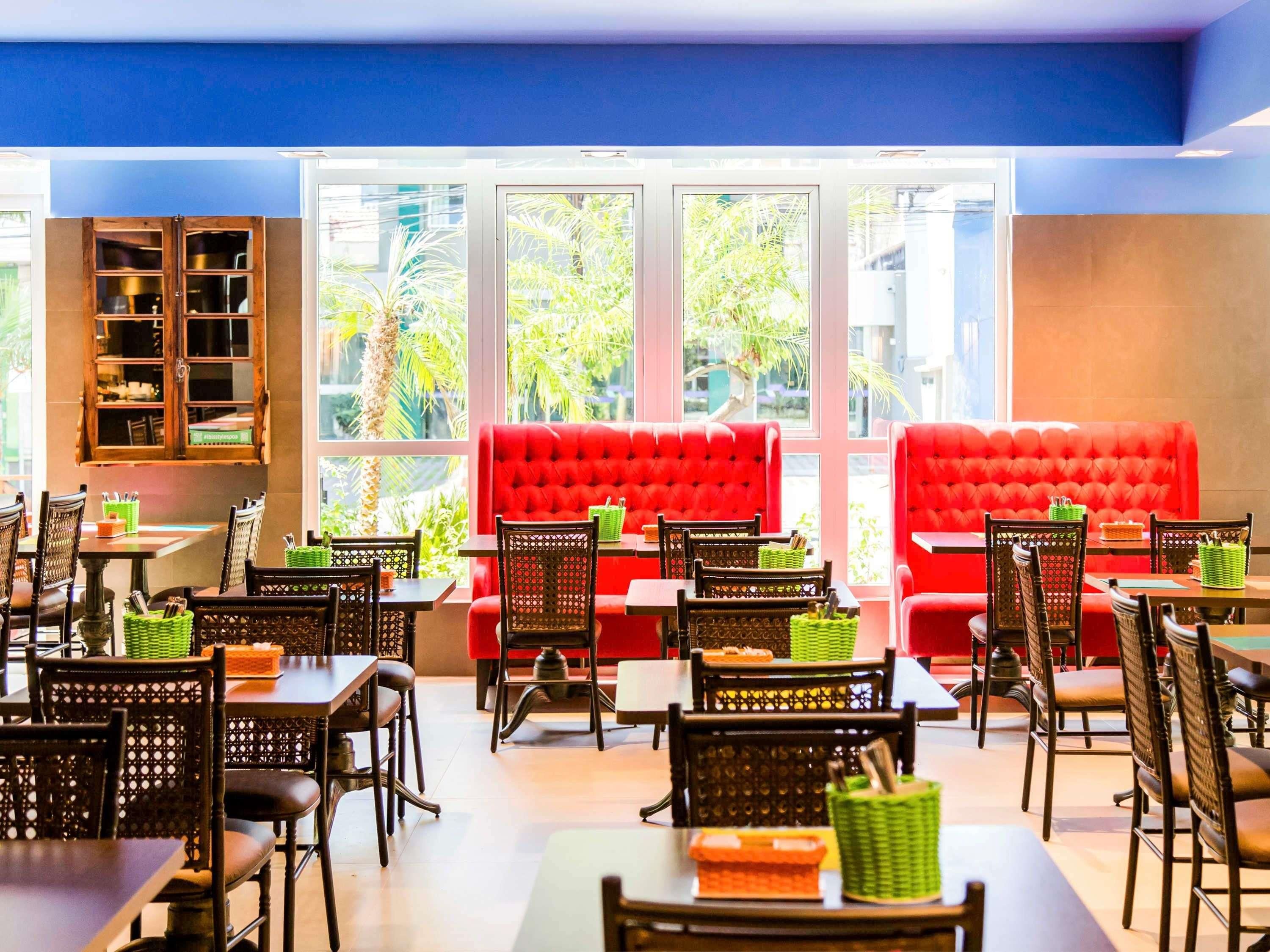 A restaurant with red cushioned seating, wooden tables, and chairs, and large windows with a view of greenery.