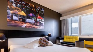 A hotel room with a large bed, a desk, a chair, and a window with curtains.