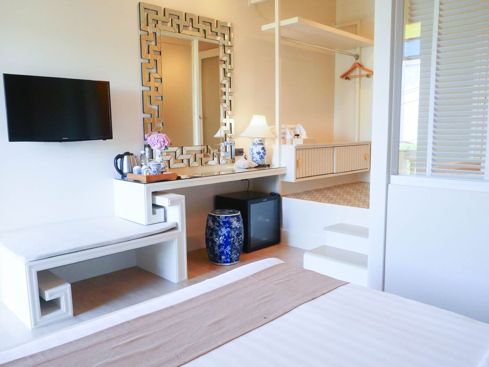 A modern hotel room with a large mirror, a flat-screen TV, a desk, and a small seating area.