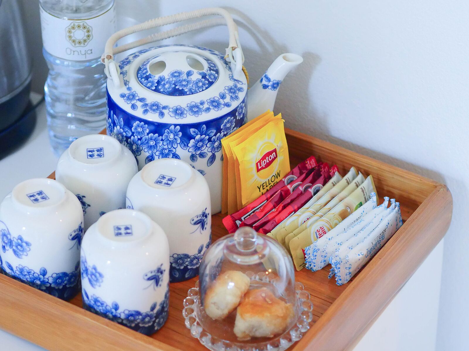 A tray with teapots, Lipton tea packets, and a glass dome with pastries.
