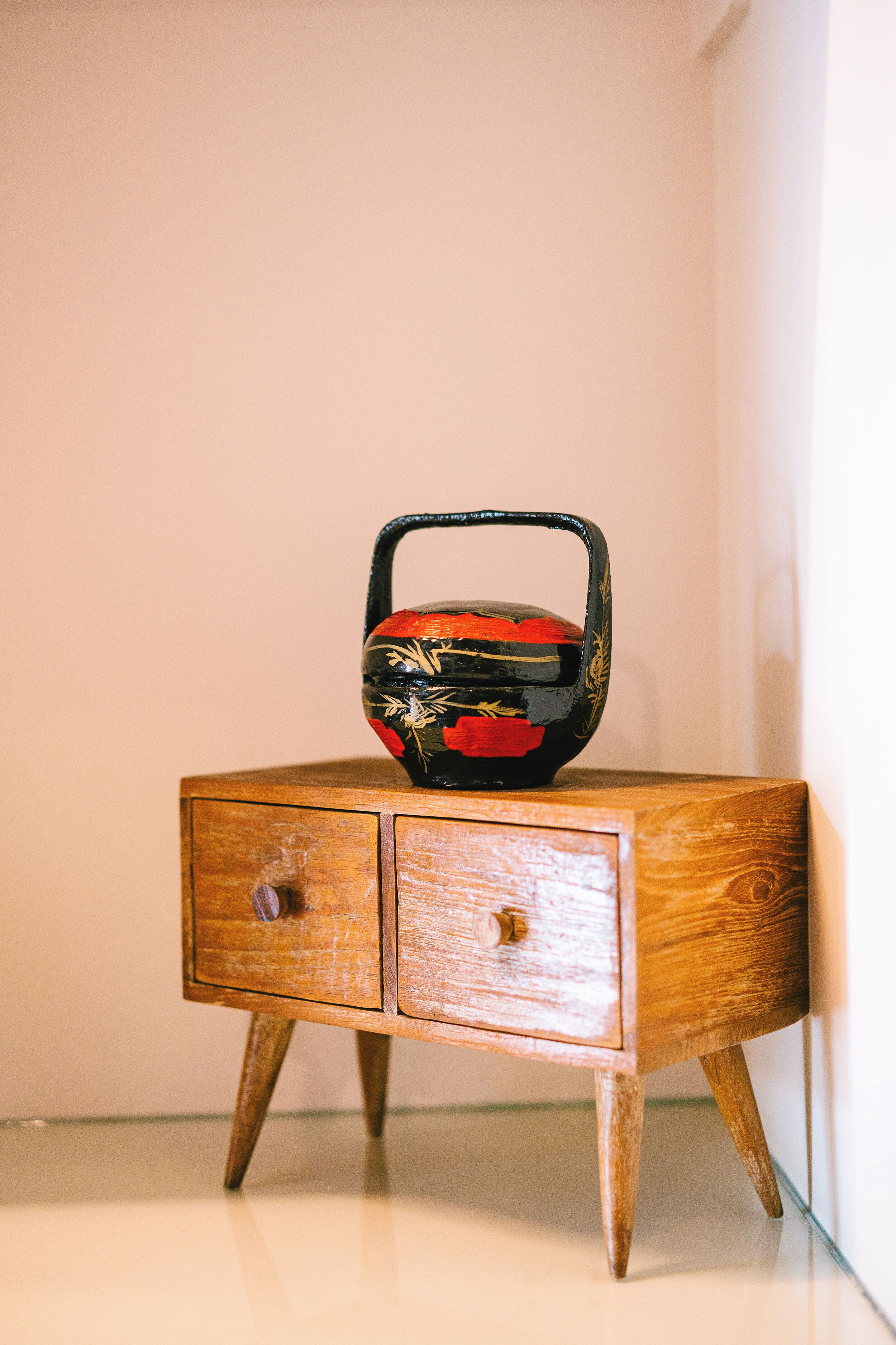 A small wooden cabinet with two drawers and a decorative vase on top.