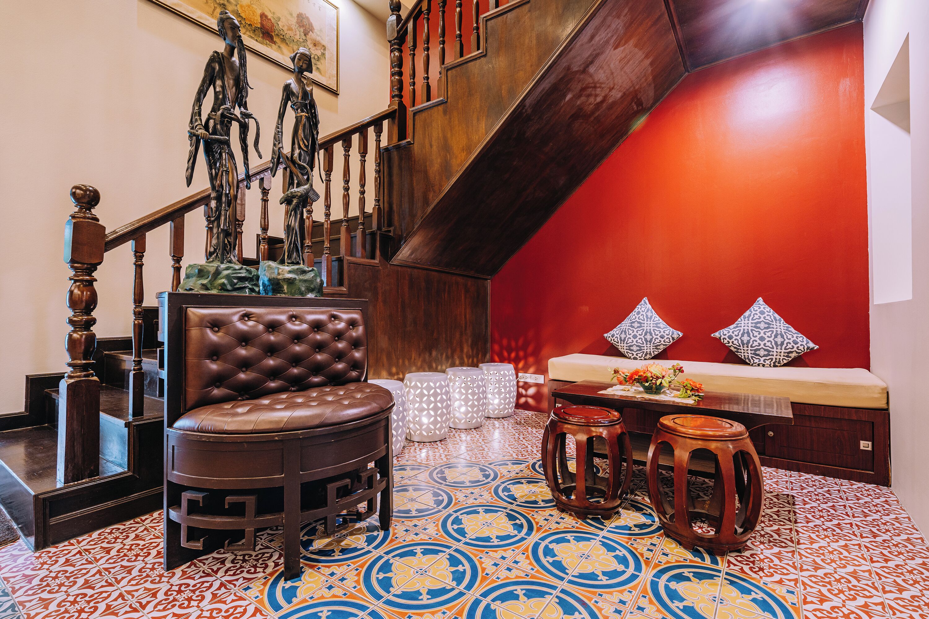 A staircase with wooden railings and a red wall. There is a brown leather chair and a wooden stool.