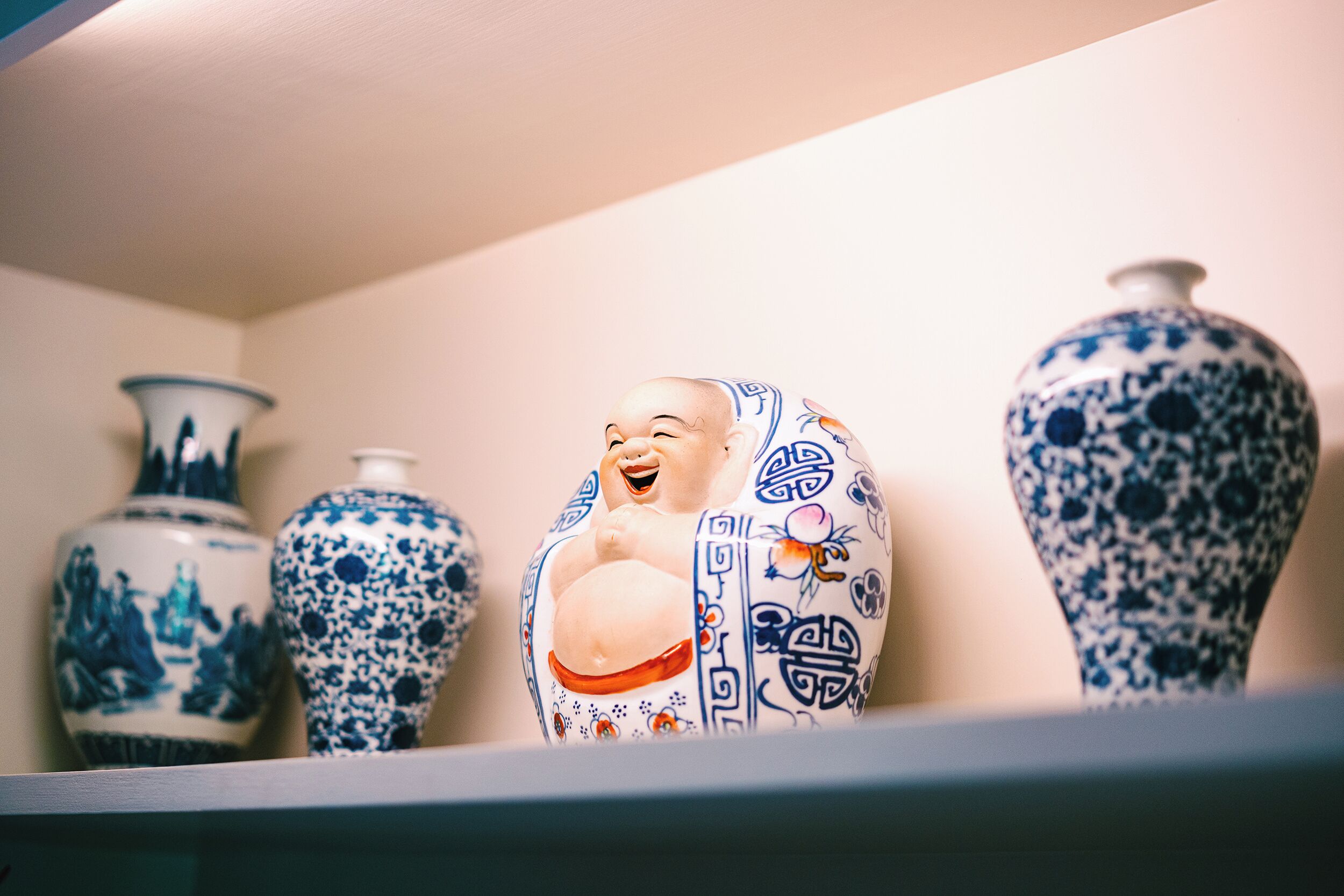A shelf with various ceramic vases, including a prominent laughing Buddha figure.
