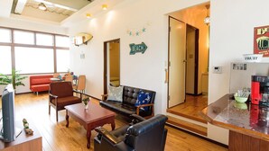 Sala de estar con sofá, sillón, mesita de centro y una zona de cocina con refrigerador y cafetera.