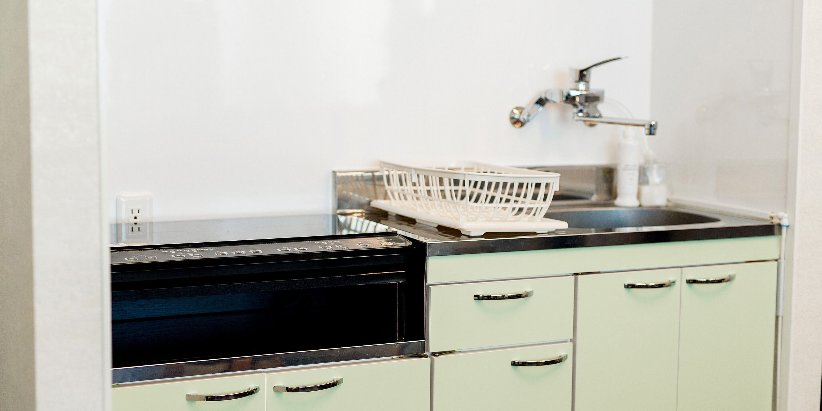 A kitchen with a black oven, a sink, and light green cabinets.