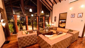Una sala de estar moderna con un sofá grande, una mesita de centro y un ventanal de vidrio que da a un balcón con plantas.
