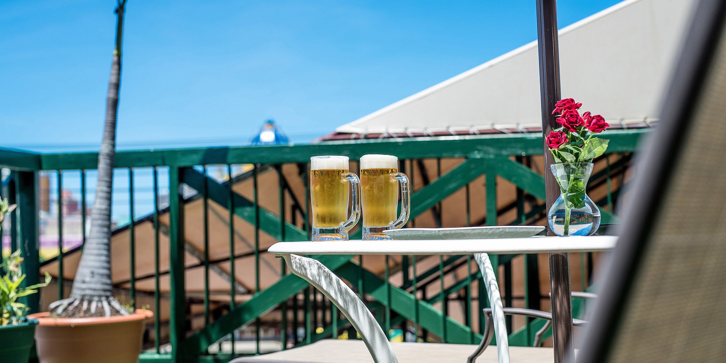 A table with two beer mugs and a vase of flowers on a balcony.