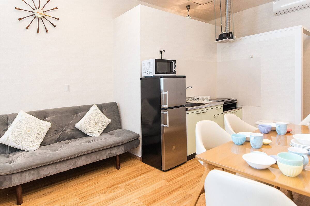 A compact living space with a kitchenette, a sofa with decorative pillows, a dining table set with bowls and plates, and a small side table.
