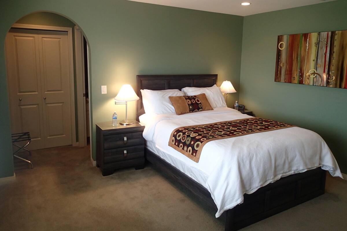A neatly made bed with a patterned throw, two bedside lamps, a water bottle, and a nightstand.