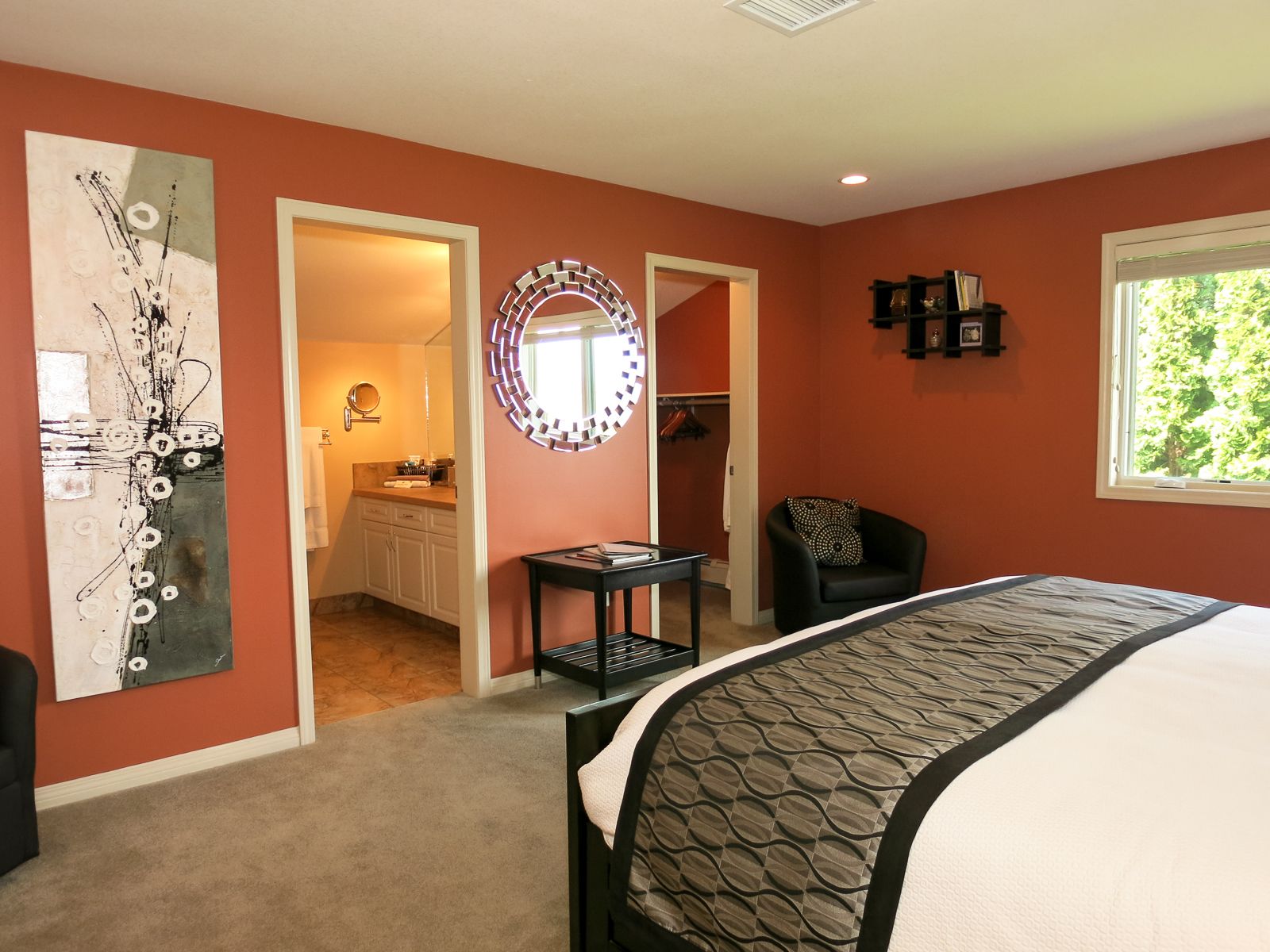 A bedroom with a bed, a chair, a desk, a mirror, and a closet.