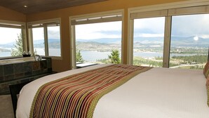 A bedroom with a large bed, a stone fireplace, and a view of a lake and mountains. - A View of the Lake Bed & Breakfast (West Kelowna)