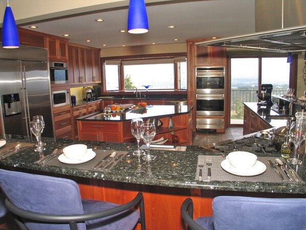 A modern kitchen with a central island, stainless steel appliances, and a view of the outdoors.