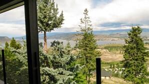 A view from a covered balcony overlooking a landscape with trees and a distant cityscape. - A View of the Lake Bed & Breakfast (West Kelowna)