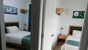 Une chambre d’hôtel avec deux lits, une tête de lit en bois, une table de chevet avec une lampe et des crochets fixés au mur.