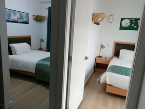 A hotel room with two beds, a wooden headboard, a nightstand with a lamp, and wall-mounted hooks. - Alpine Inn & Suites (Revelstoke)