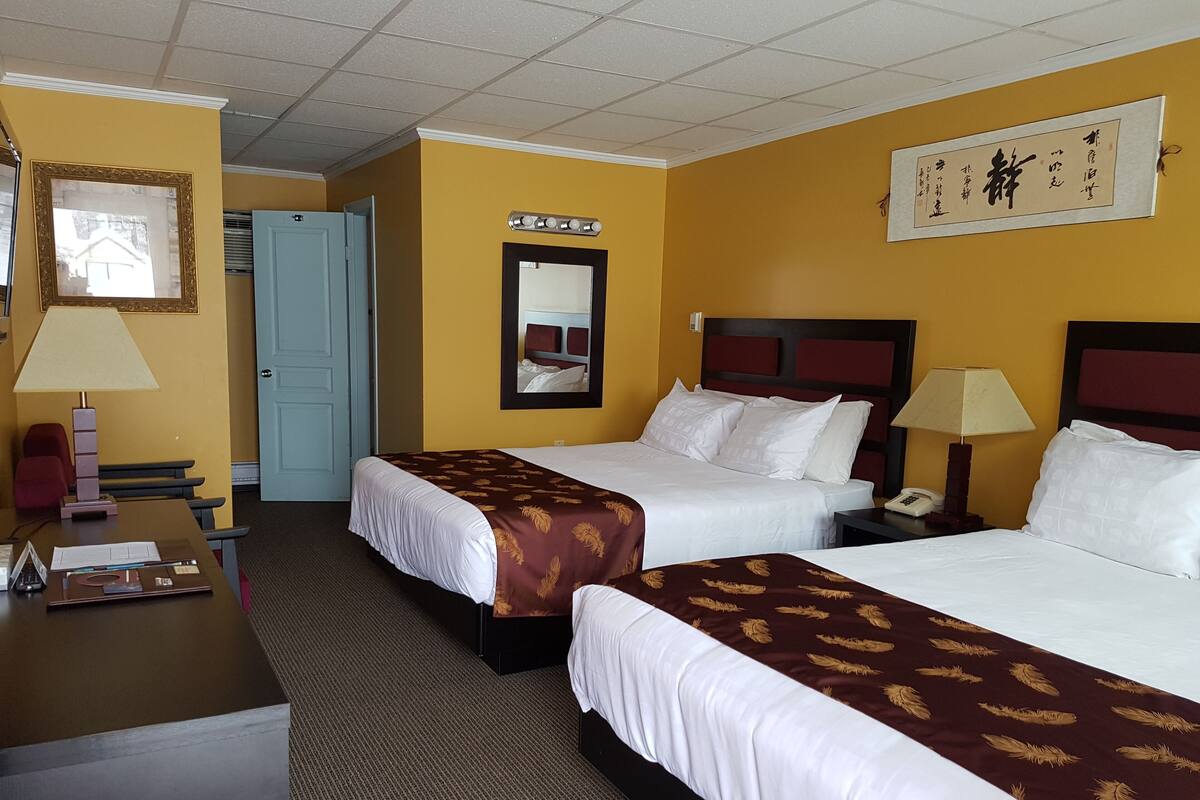 A hotel room with two beds, a desk, a chair, a lamp, a telephone, and a mirror.