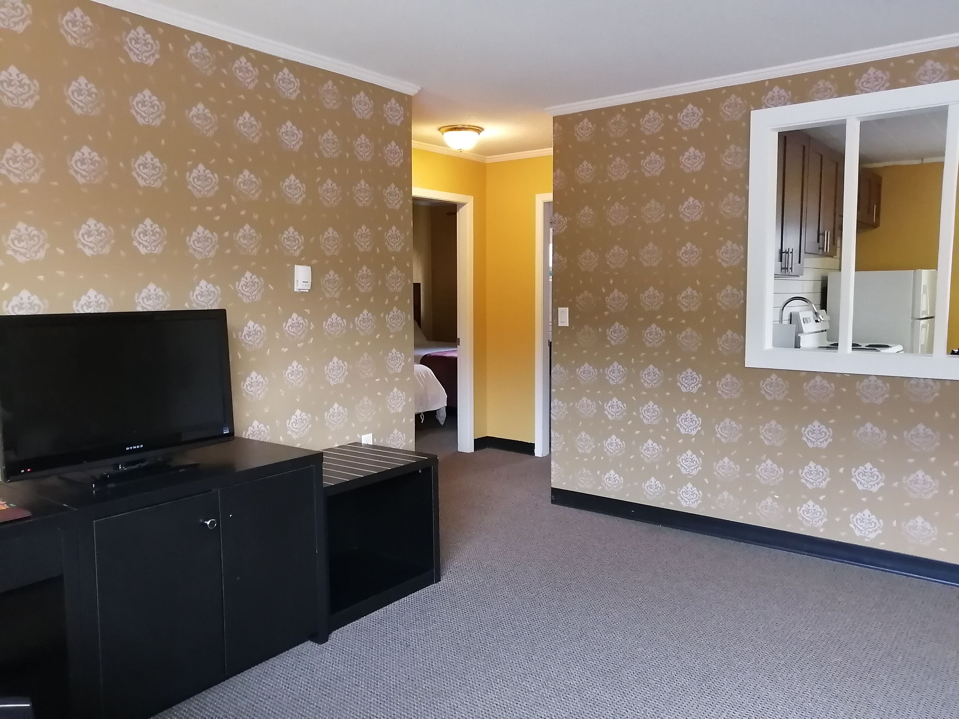 A hotel room with patterned wallpaper, a flat-screen TV, a black entertainment unit, and a large mirror.
