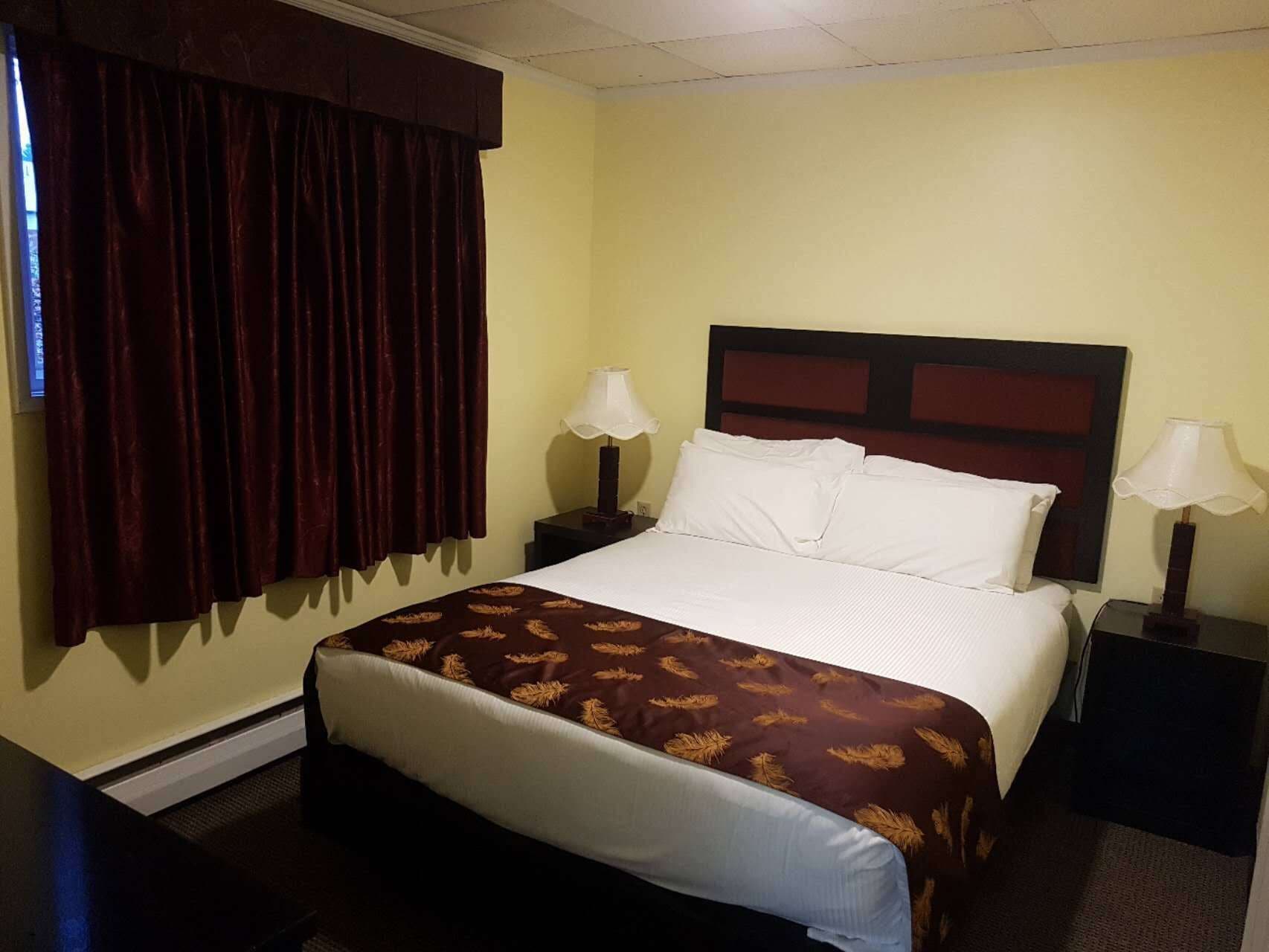 A hotel room with a large bed, two bedside tables with lamps, a window with curtains, and a carpeted floor.