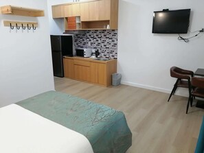 A compact kitchen with wooden cabinets, a microwave, and a sink. There is a TV mounted on the wall and a small trash bin.
