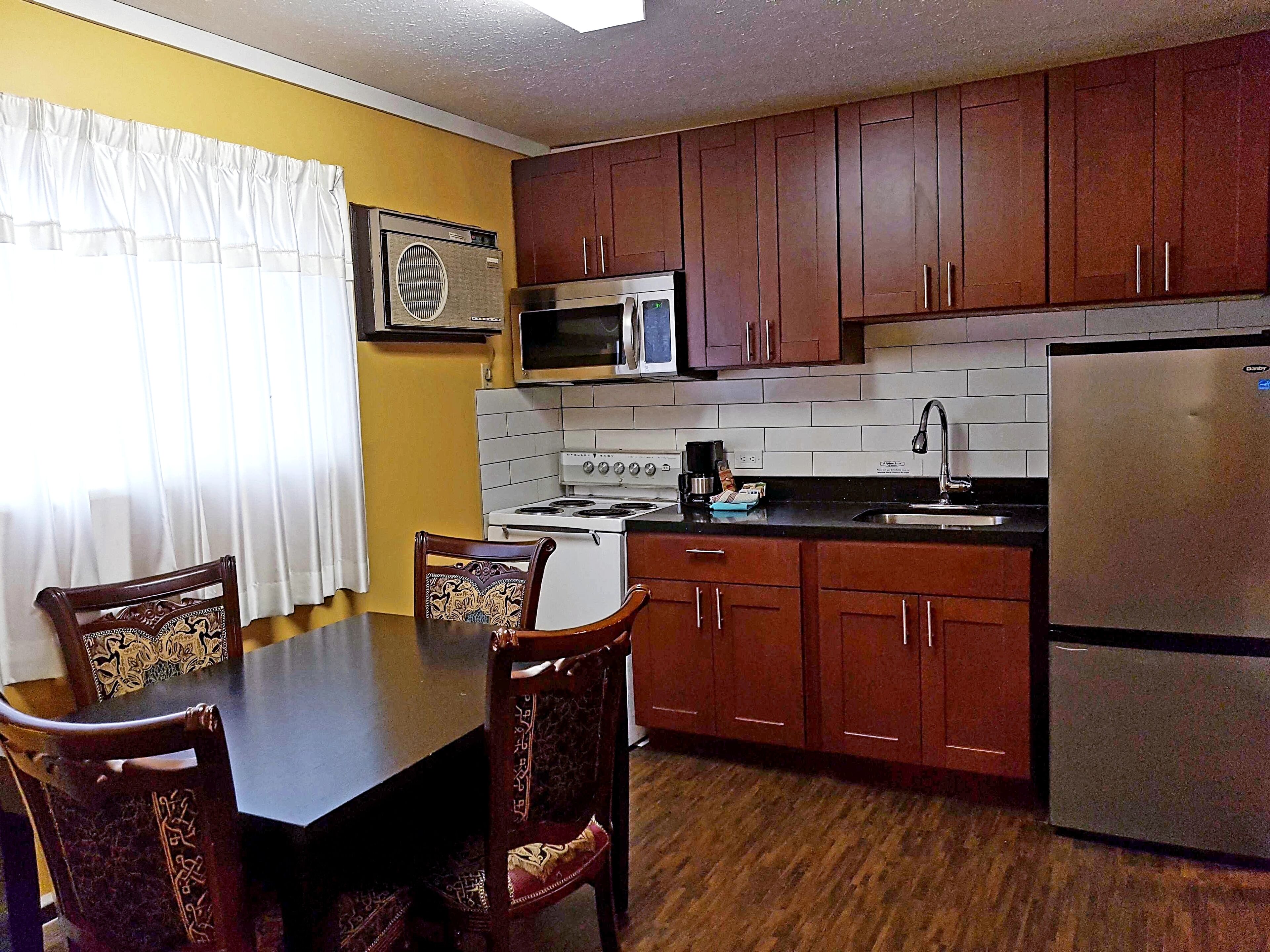 Cocina compacta con armarios de madera, microondas, estufa y refrigerador.