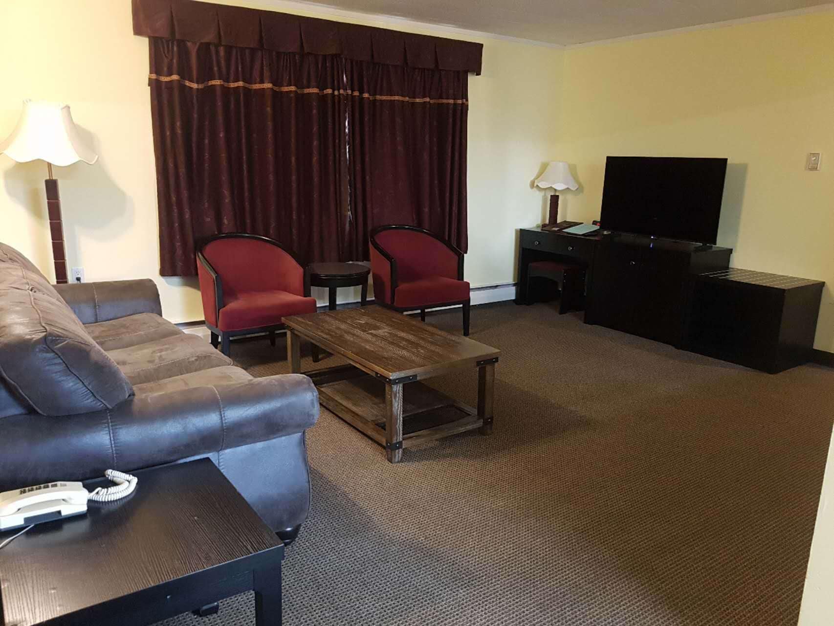 A hotel room with a sofa, two armchairs, a coffee table, a desk with a flat-screen TV, and lamps.