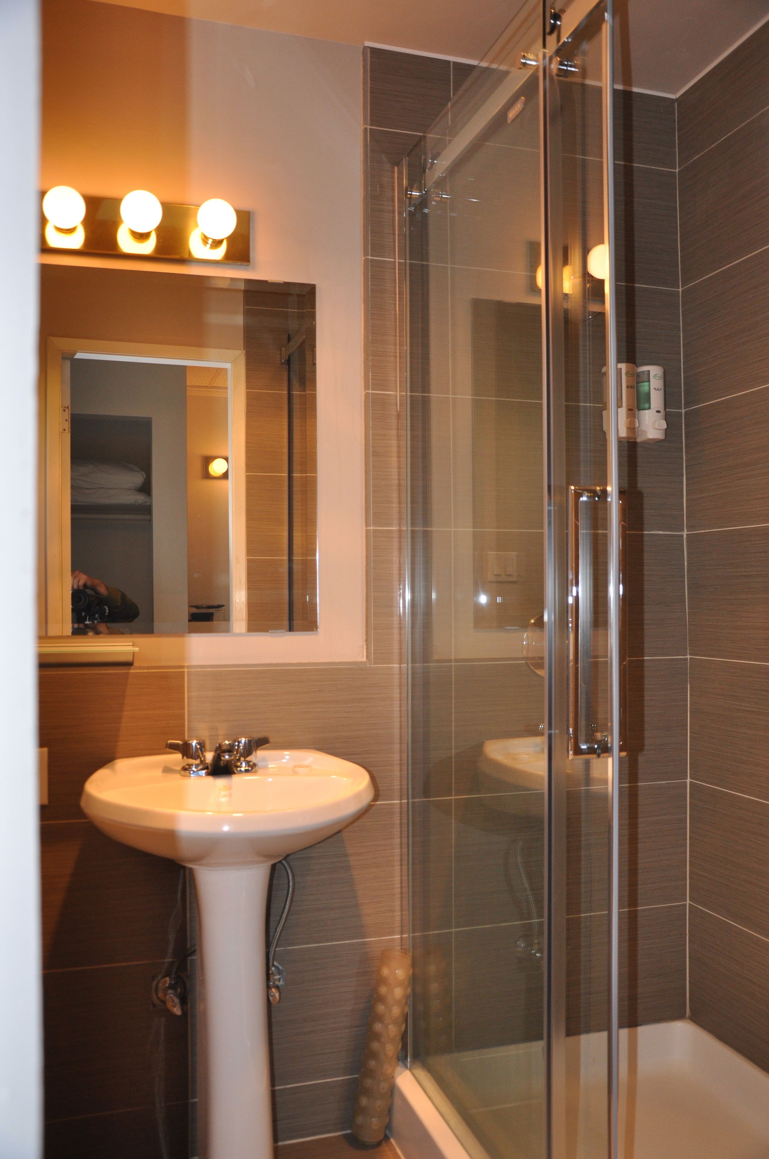 A bathroom with a glass-enclosed shower, a sink, and a mirror with lights above.