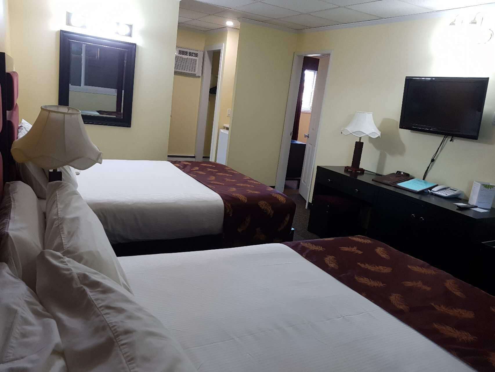 Een hotelkamer met twee bedden, een bureau met lamp, een televisie en een deur naar een andere kamer.
