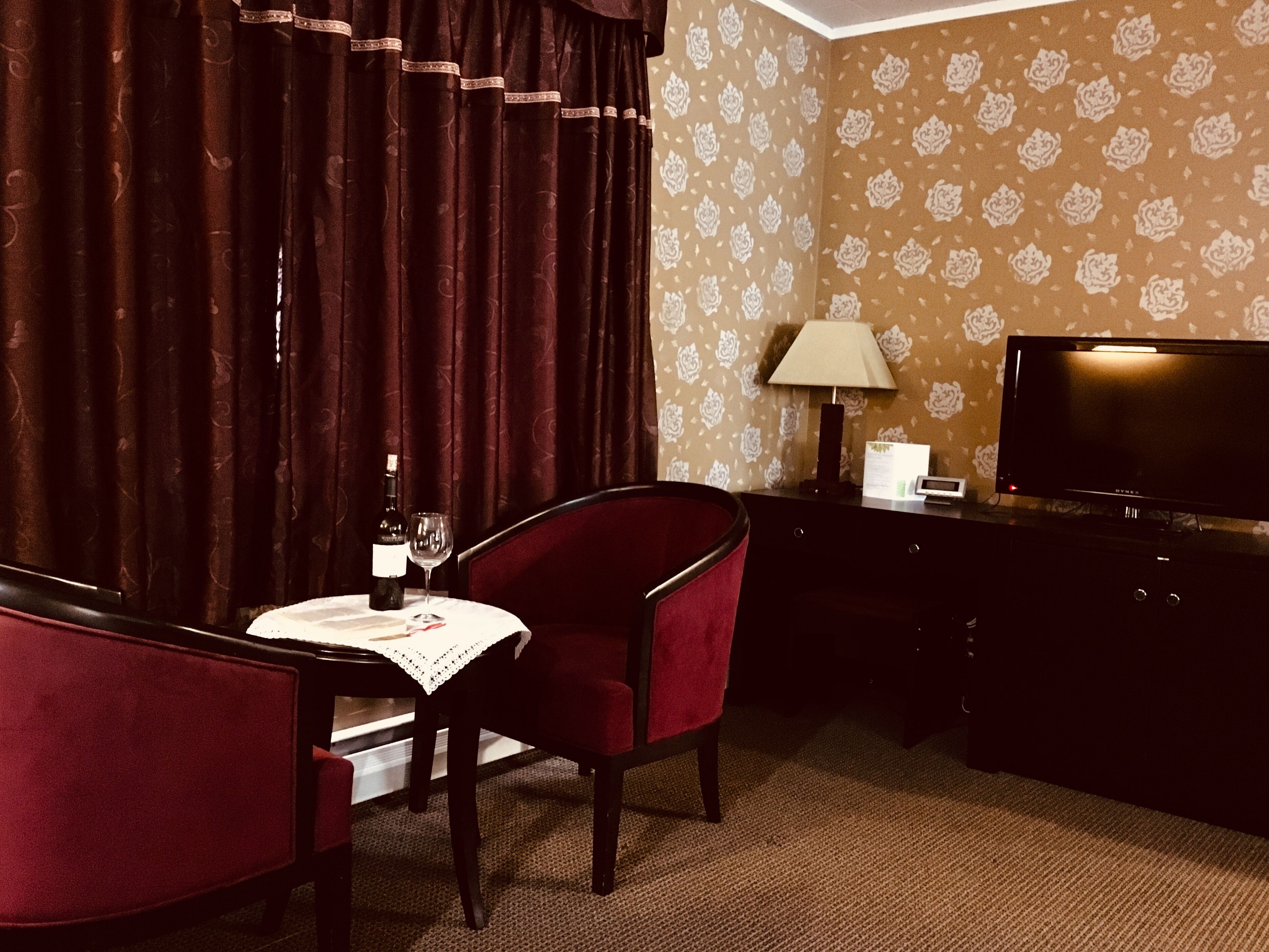 Hotelkamer met een eettafel, een stoel, een fles wijn en een televisietoestel op een standaard.