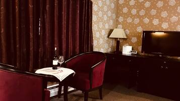 Hotelkamer met een eettafel, een stoel, een fles wijn en een televisietoestel op een standaard.