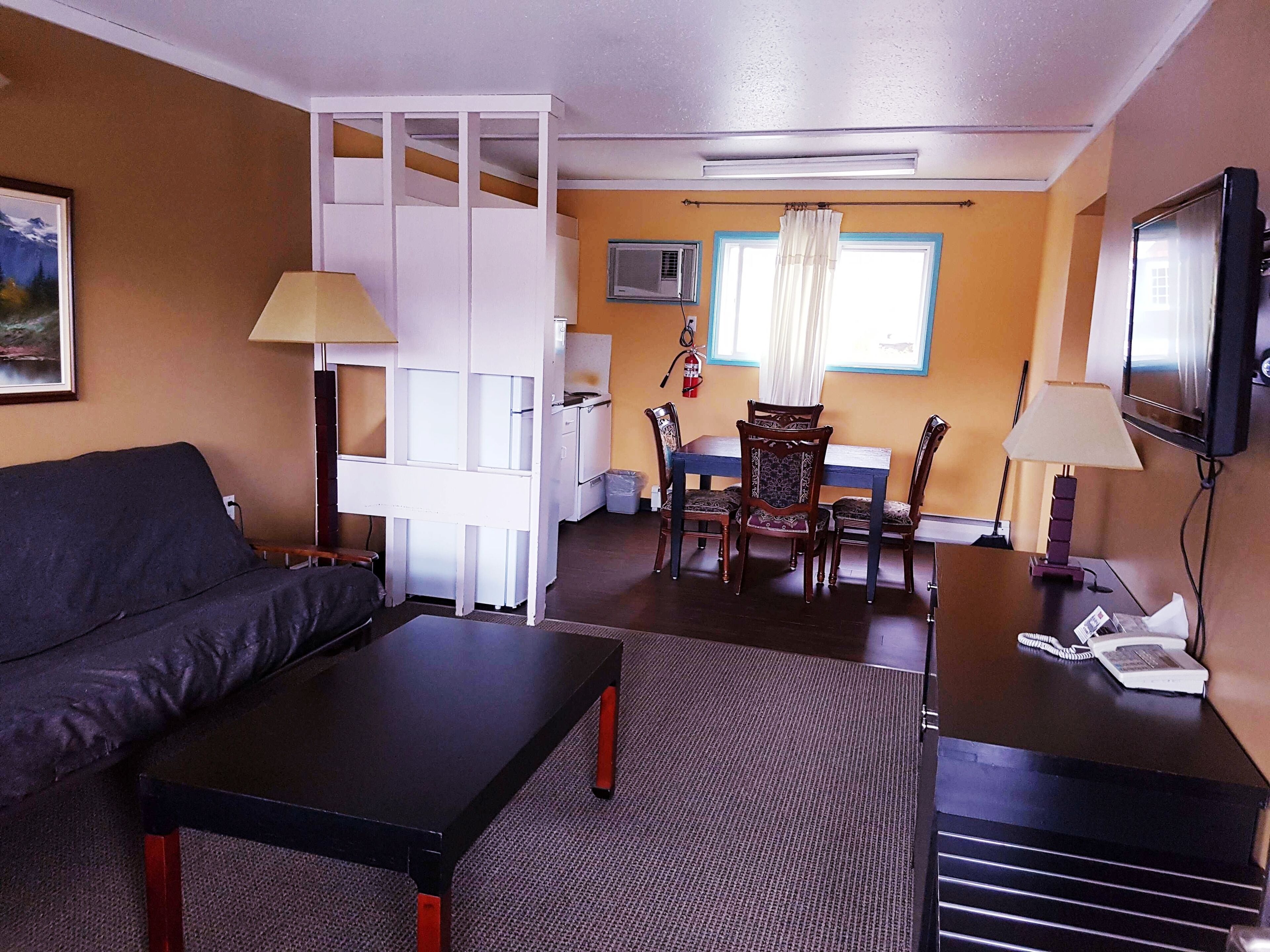 A hotel room with a sofa, a dining table with chairs, a TV, a lamp, and a telephone.