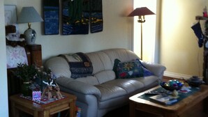 A living room with a sofa, a coffee table, a lamp, and a painting on the wall. - Calla's Palace (Jasper)