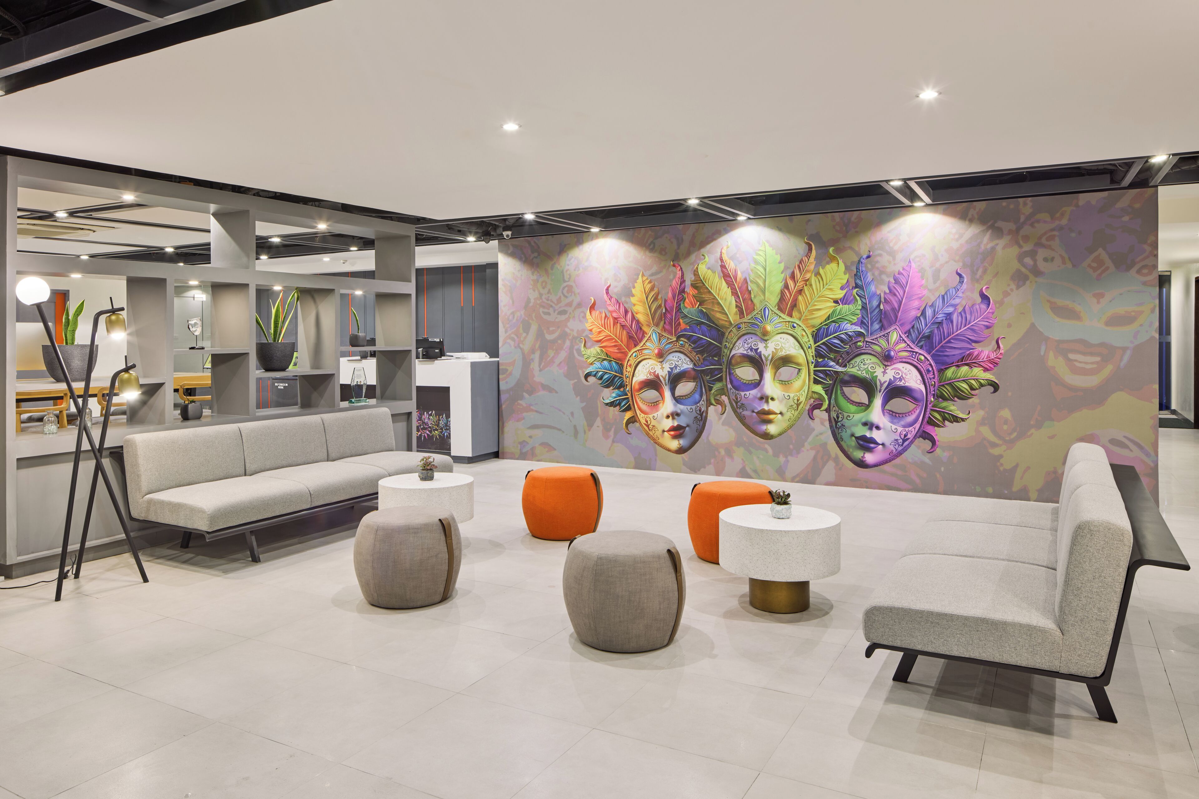 Een moderne lobby met een grijze bank, oranje poefs en een kleurrijke muurschildering.