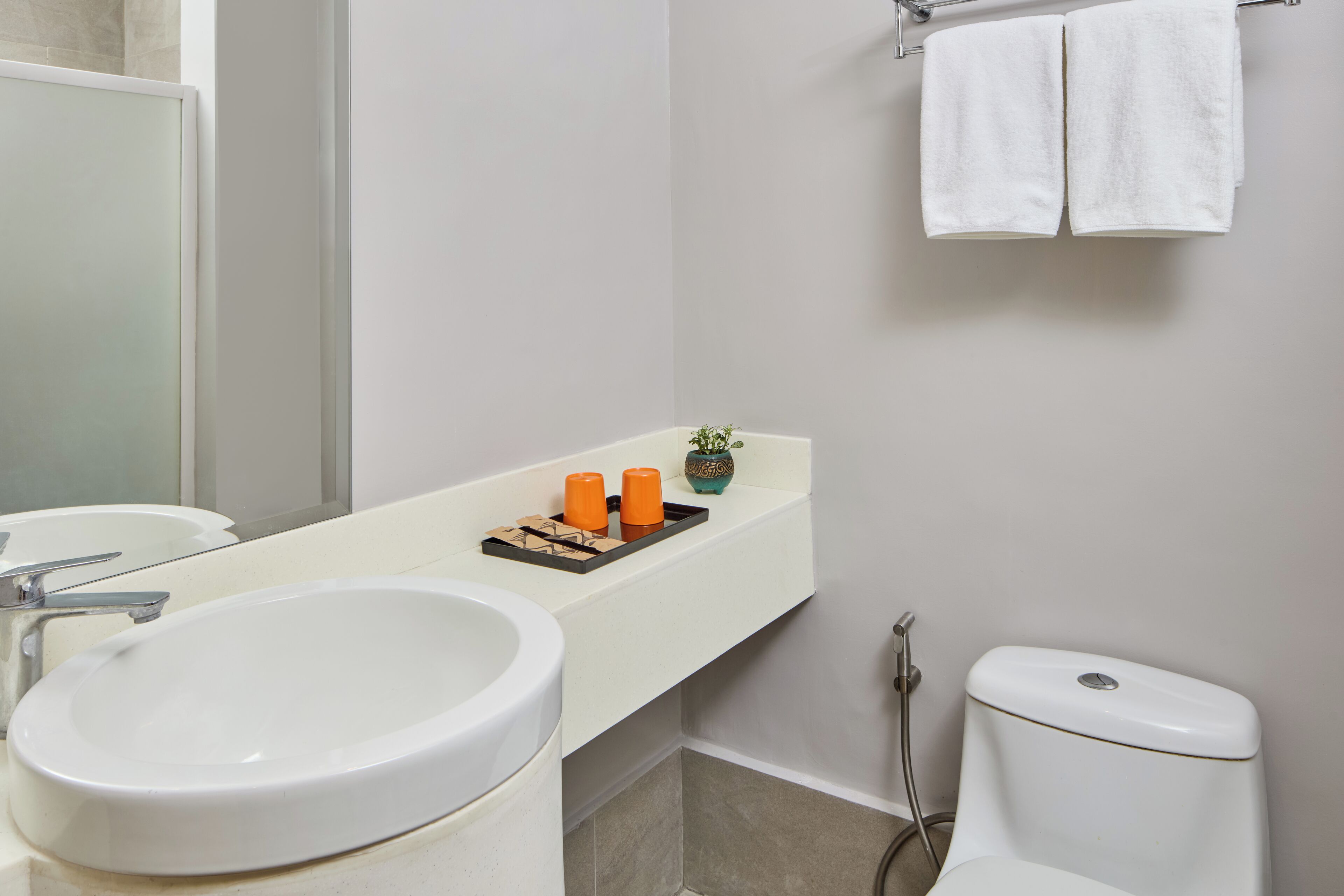 Un baño con lavamanos blanco, un espejo, un inodoro y un toallero con dos toallas.