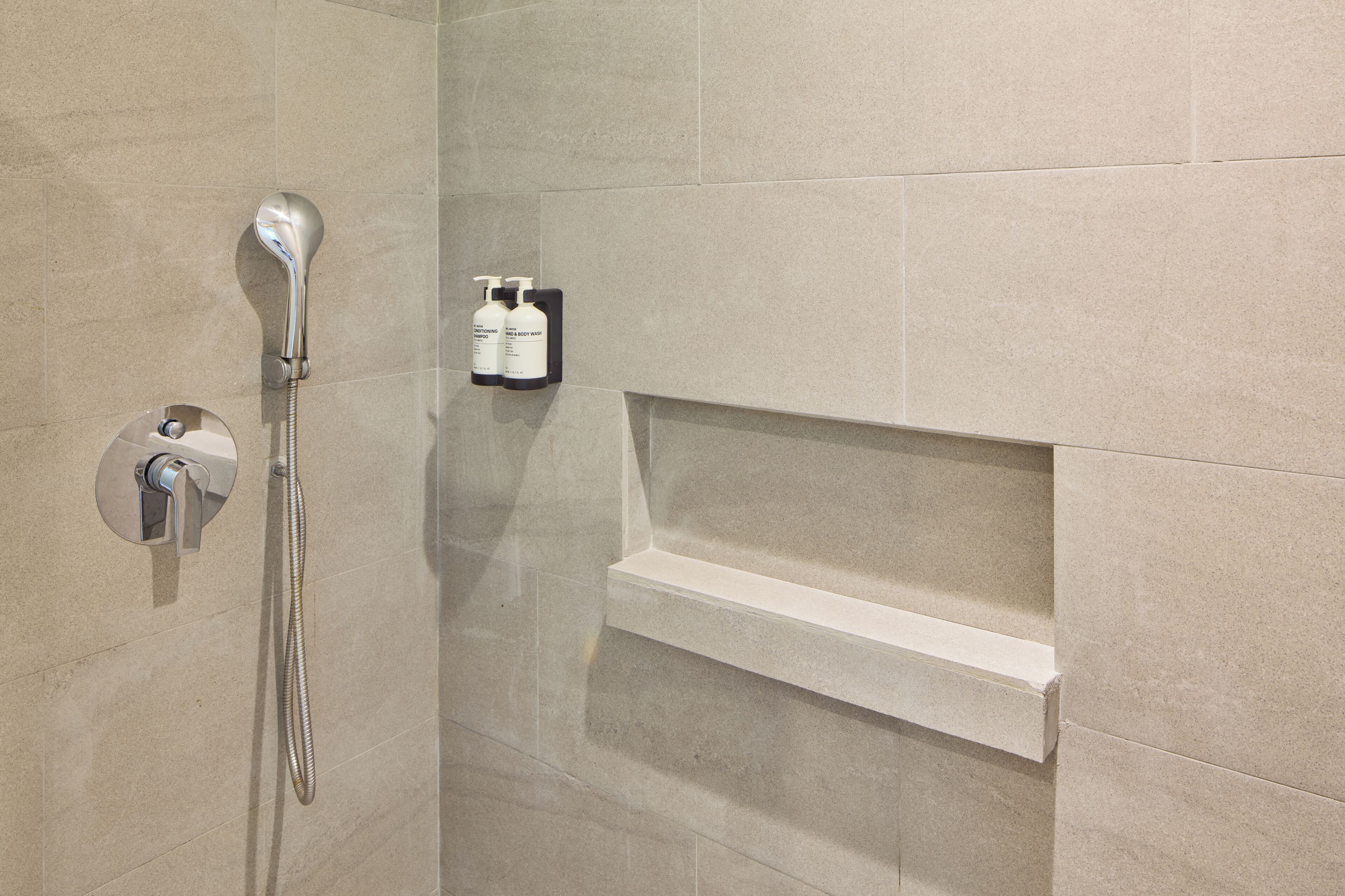 A shower area with a handheld showerhead, a wall-mounted faucet, and a shelf with toiletries.
