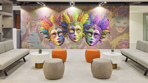 A modern lobby with a colorful mural of masks, grey sofas, and round tables with small potted plants. - Go Hotels Plus Bacolod Newly Renovated (Bacolod)
