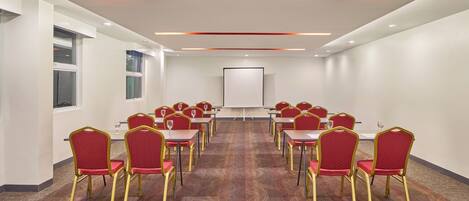 Un salón de conferencias con filas de sillas rojas, una pizarra y suelo alfombrado.