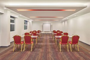 Un salón de conferencias con filas de sillas rojas, una pizarra y suelo alfombrado.