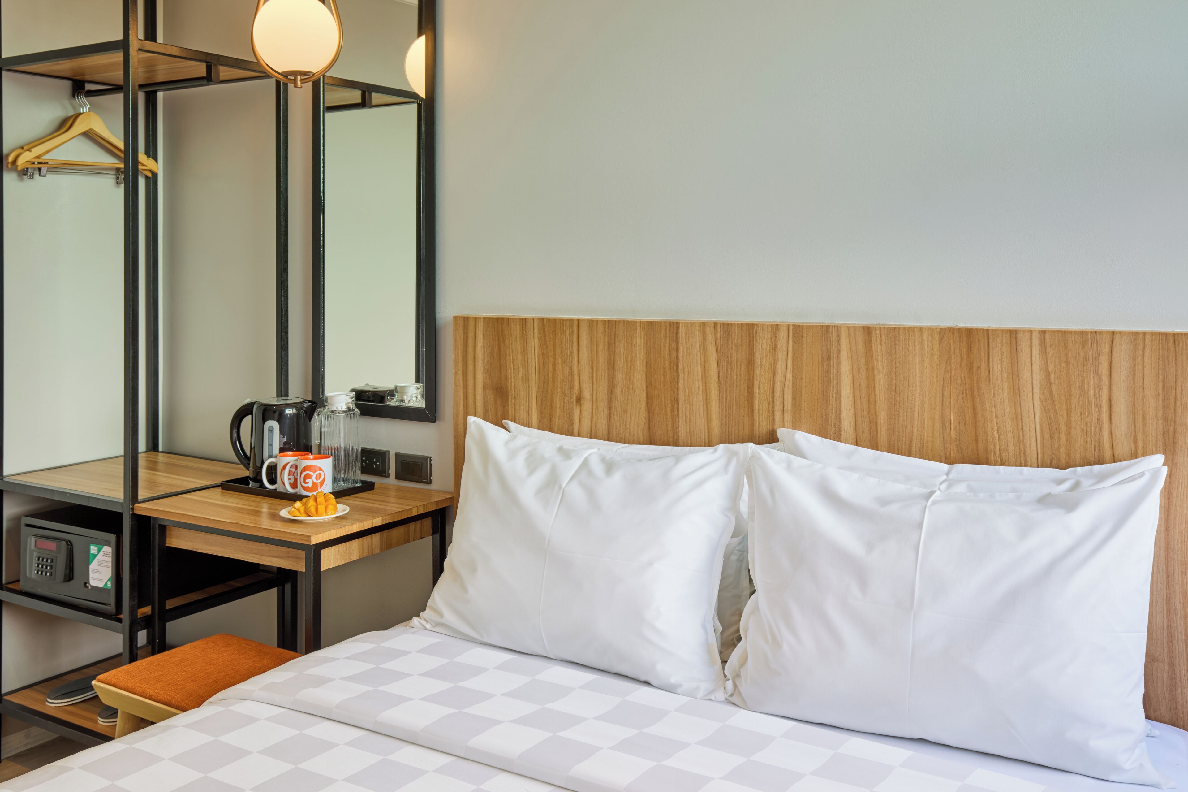 Habitació d'hotel amb un llit, un panell de capçalera de fusta, una taula de nit amb una cafetera, una tassa i un plat de fruita.