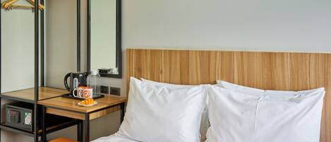 Quarto de hotel com uma cama, cabeceira de madeira, mesa de cabeceira com cafeteira, caneca e prato de frutas.