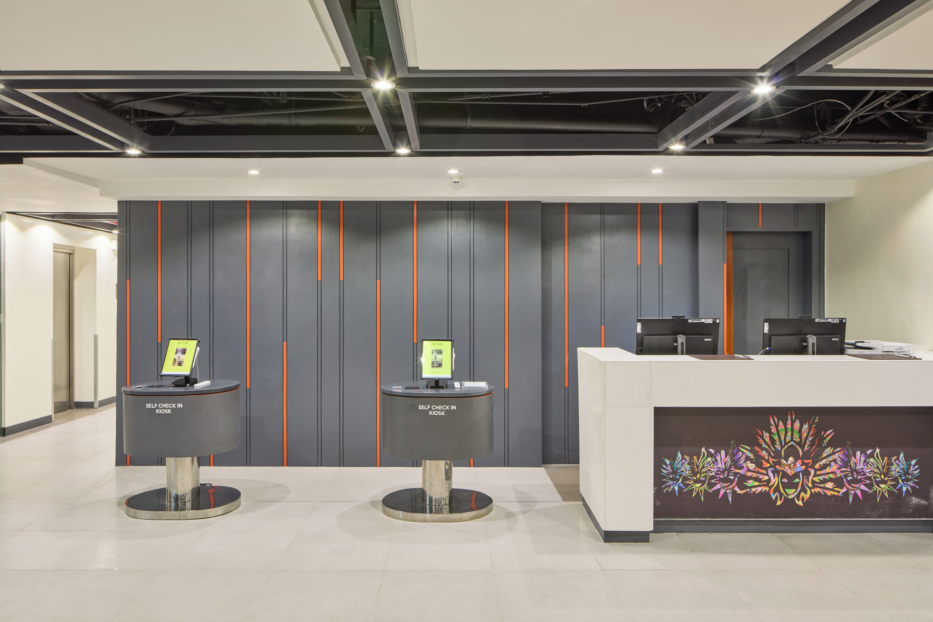 A self-check-in kiosk area with two kiosks, a reception desk, and a decorative wall.