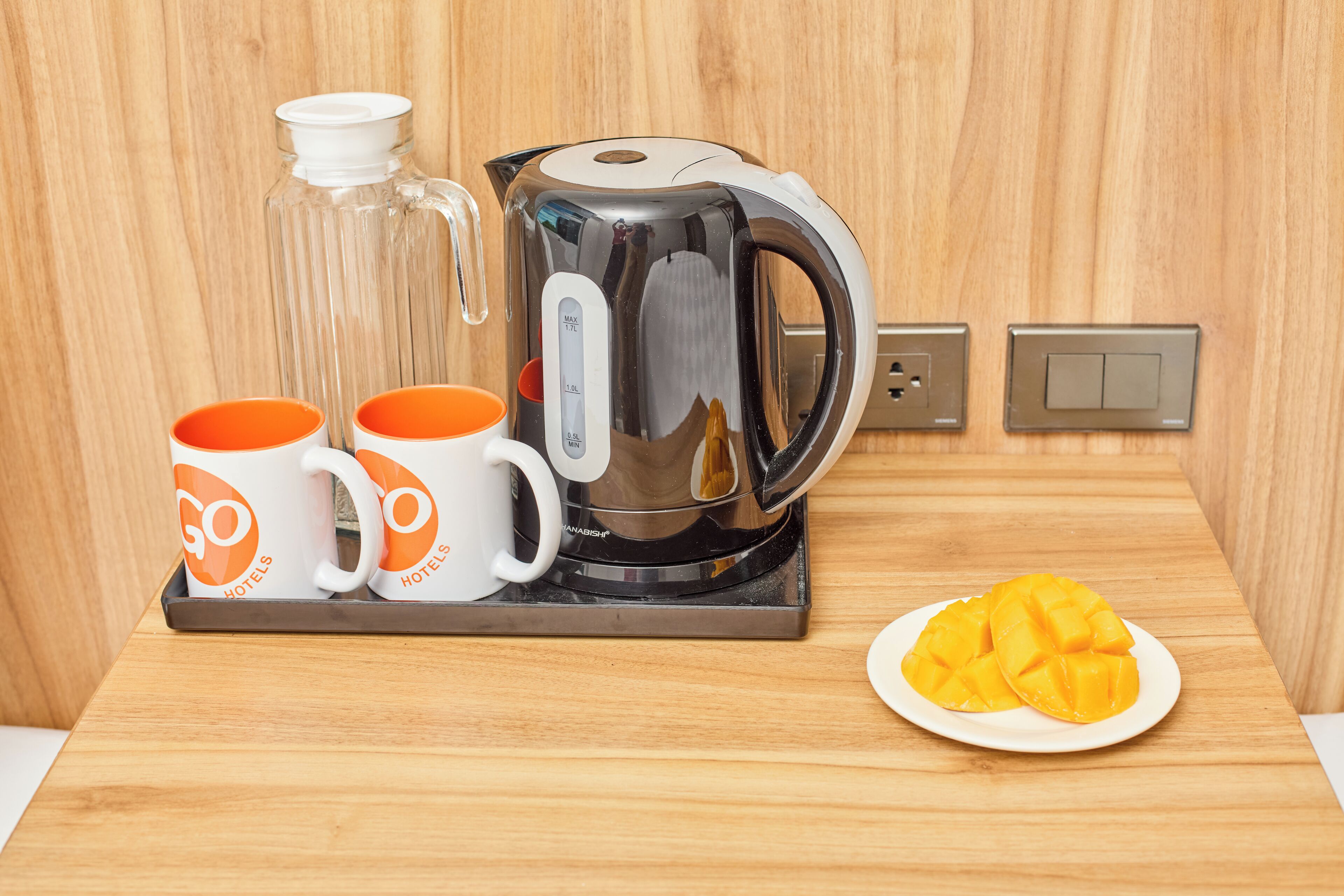 A kitchen area with a coffee maker, two mugs, a glass carafe, and a plate of fruit.