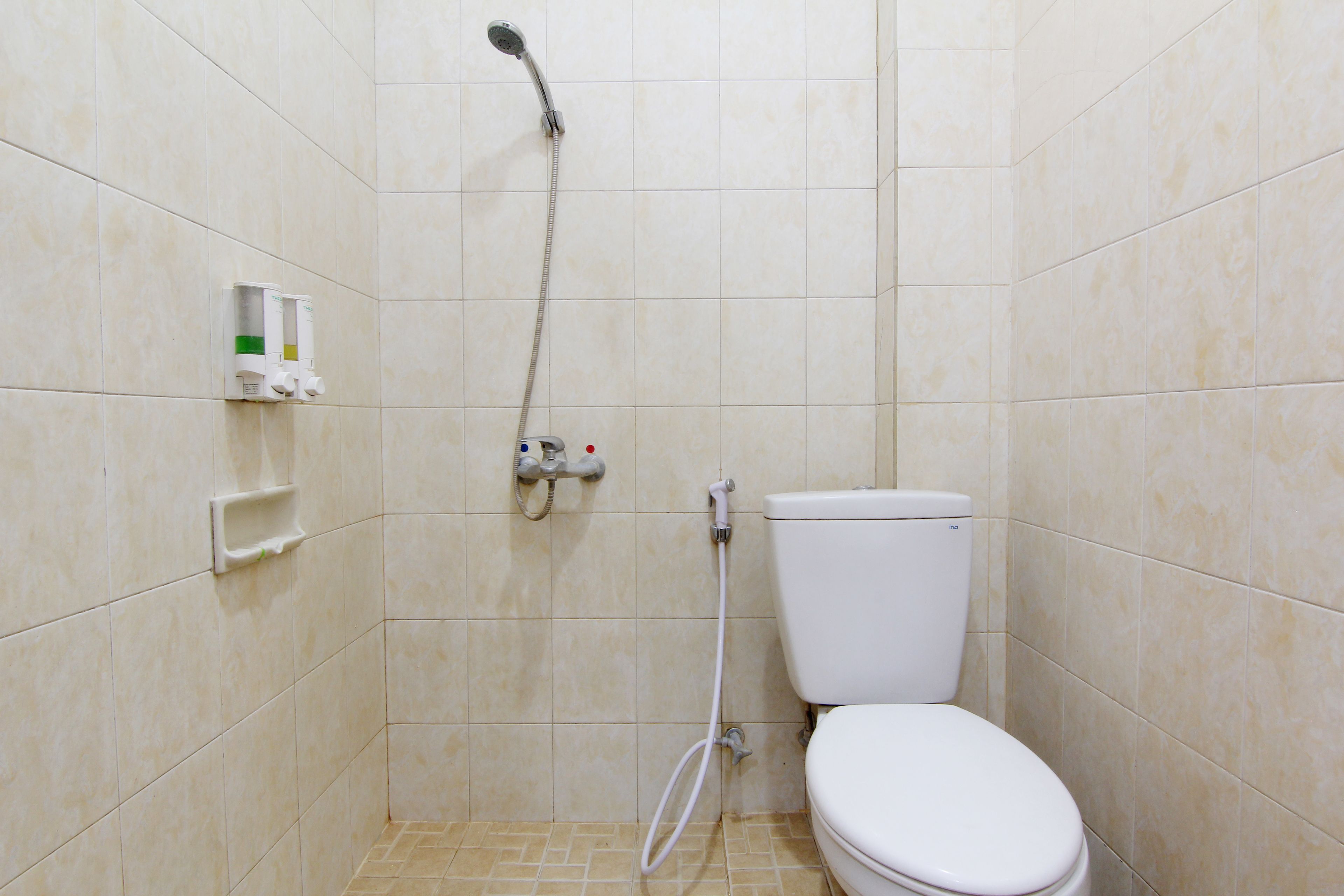 A small, tiled bathroom with a toilet, a showerhead, and a soap dispenser.