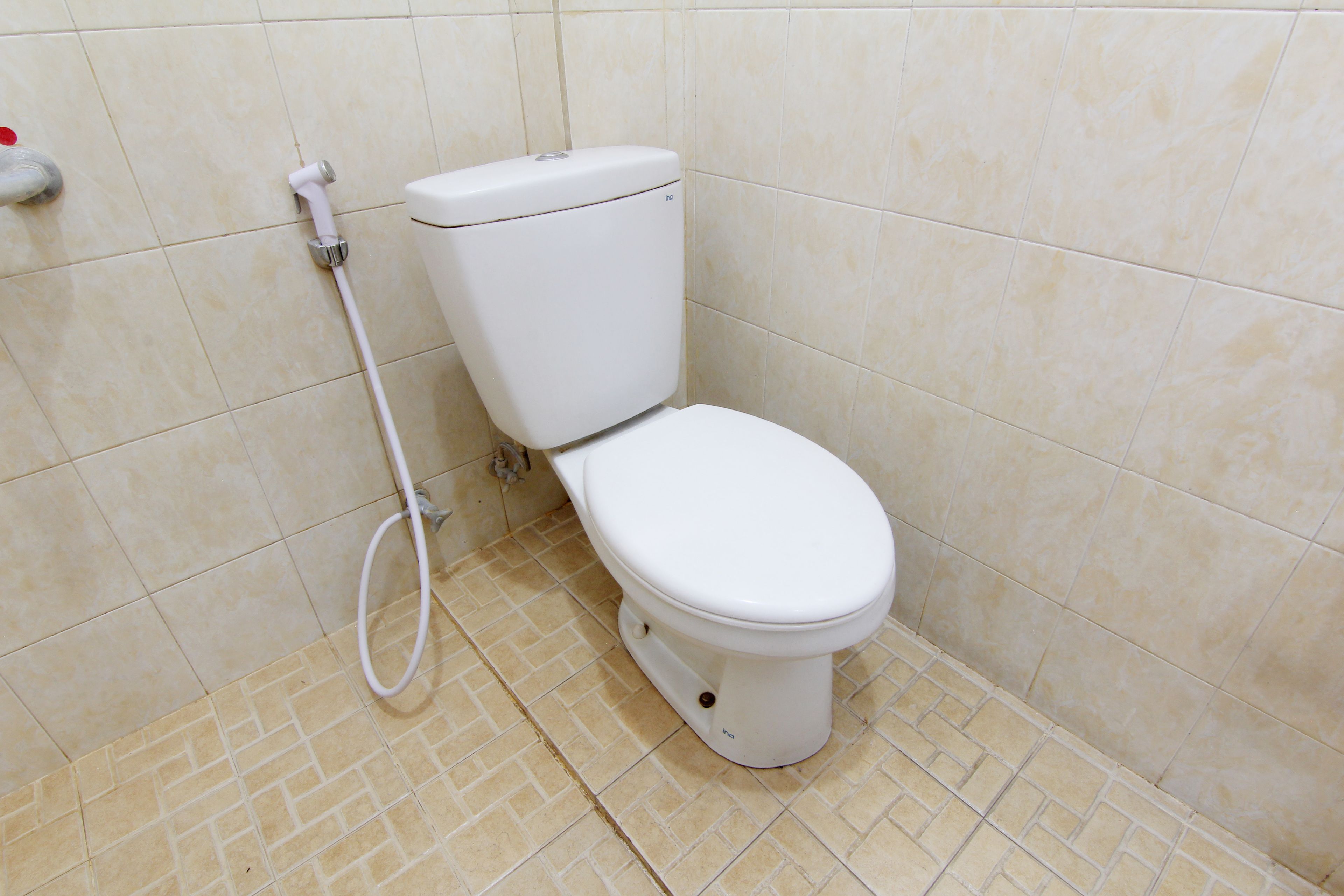 A white toilet with a bidet attachment in a bathroom with beige tiled walls and floor.