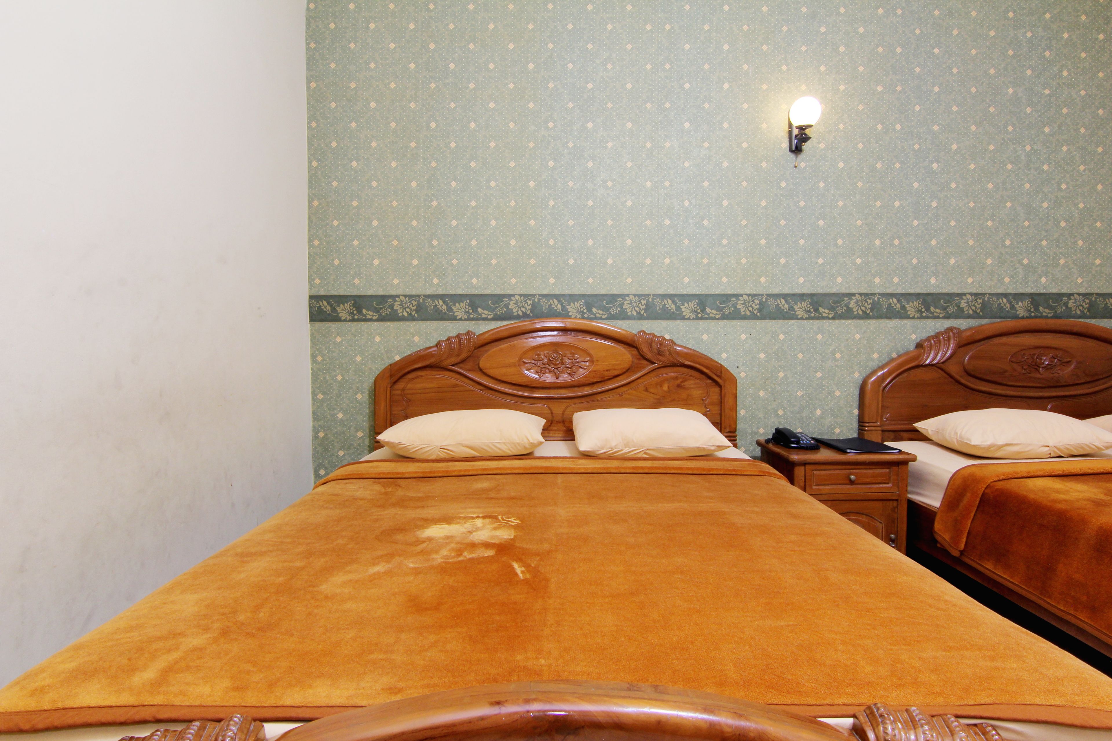A double bed with a wooden headboard, a bedside table with a lamp, and a patterned wall.